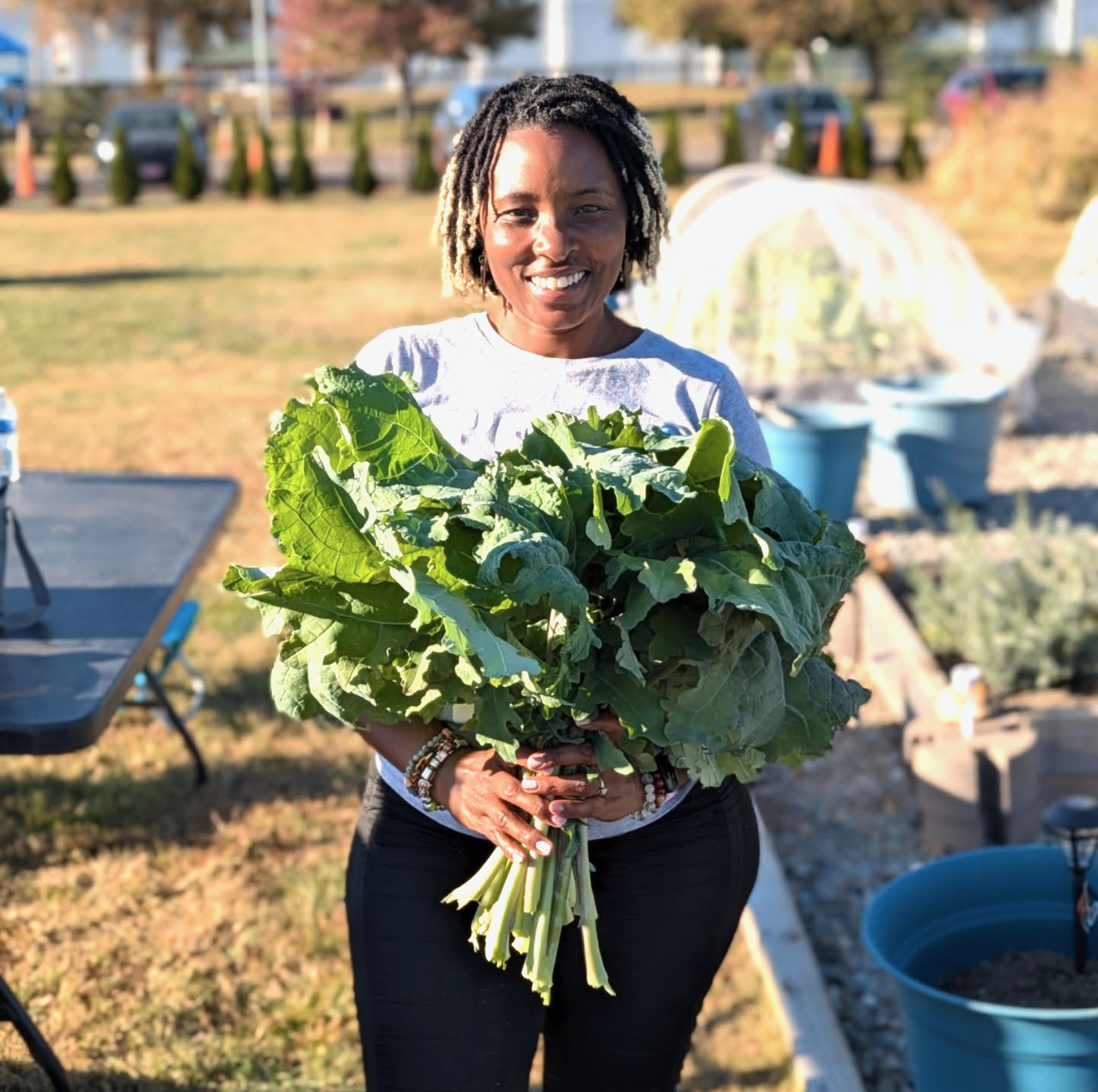 Stacey Woodson holding fresh greens in a community garden.